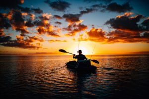 A silhouette of a person in a kayak on the sea during sunset